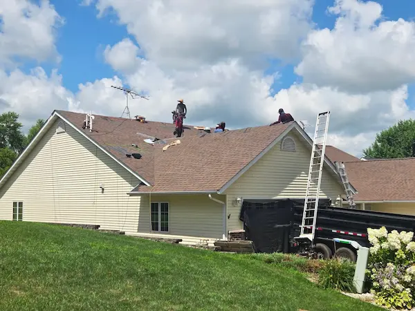 Roofing crew installing brown architectural shingles on a residential home with multiple valleys and roof sections