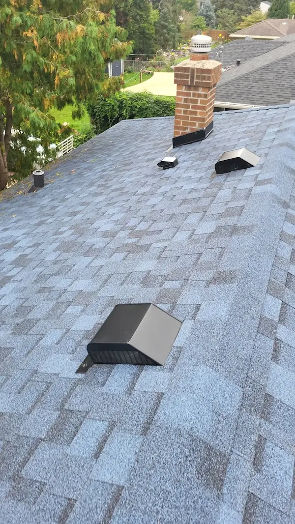 Completed light gray architectural shingle roof with box vents pipe flashing and metal roof vents
