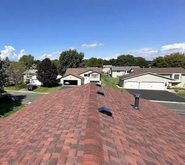 Completed residential roof replacement with red-brown architectural shingles and multiple roof vents